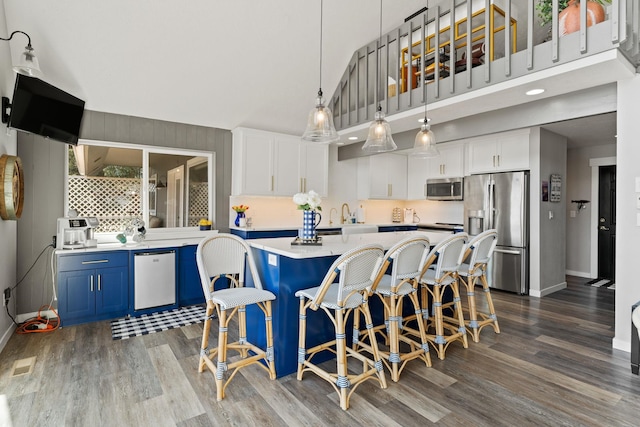 kitchen featuring stainless steel appliances, blue cabinets, hanging light fixtures, white cabinets, and a breakfast bar