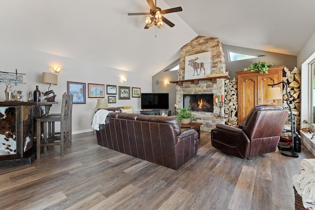 living room with ceiling fan, dark hardwood / wood-style floors, a stone fireplace, and vaulted ceiling