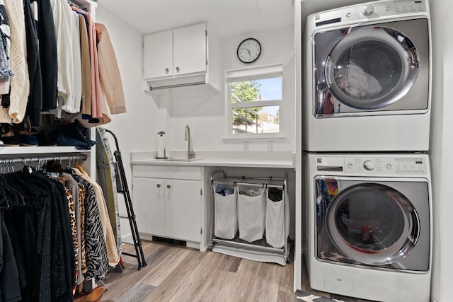 laundry area featuring stacked washer / drying machine, light wood-type flooring, sink, and cabinets