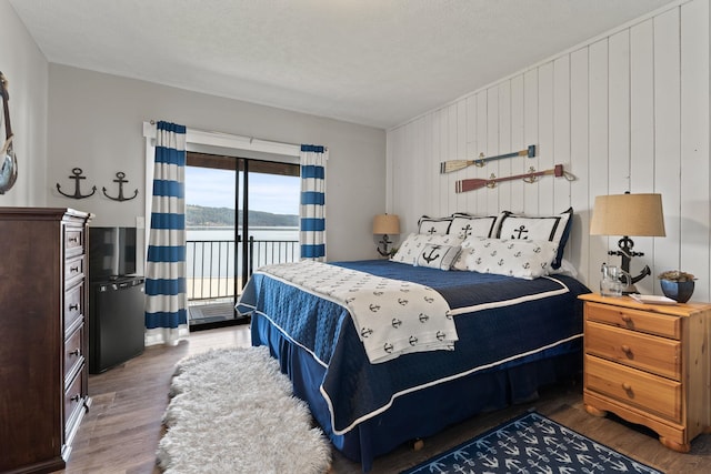 bedroom with wooden walls, a textured ceiling, dark hardwood / wood-style floors, and access to outside