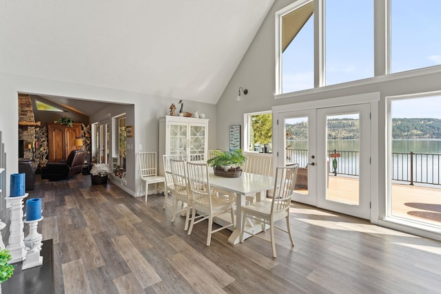 dining area featuring hardwood / wood-style floors, a water view, french doors, and high vaulted ceiling