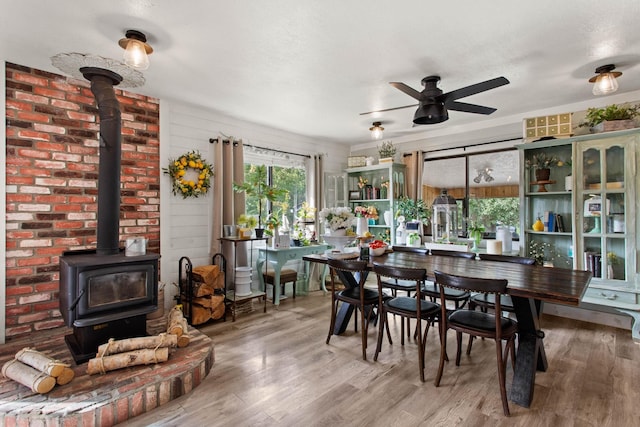 dining room with ceiling fan, a wood stove, and hardwood / wood-style flooring