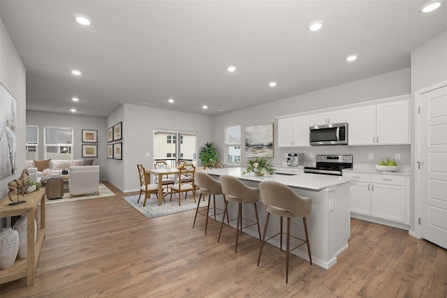 kitchen featuring light hardwood / wood-style floors, a center island, white cabinetry, a breakfast bar area, and stainless steel appliances