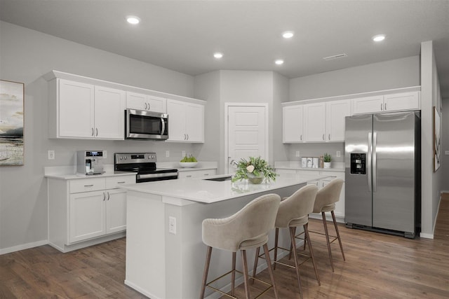 kitchen featuring a kitchen island with sink, appliances with stainless steel finishes, white cabinetry, and a kitchen bar