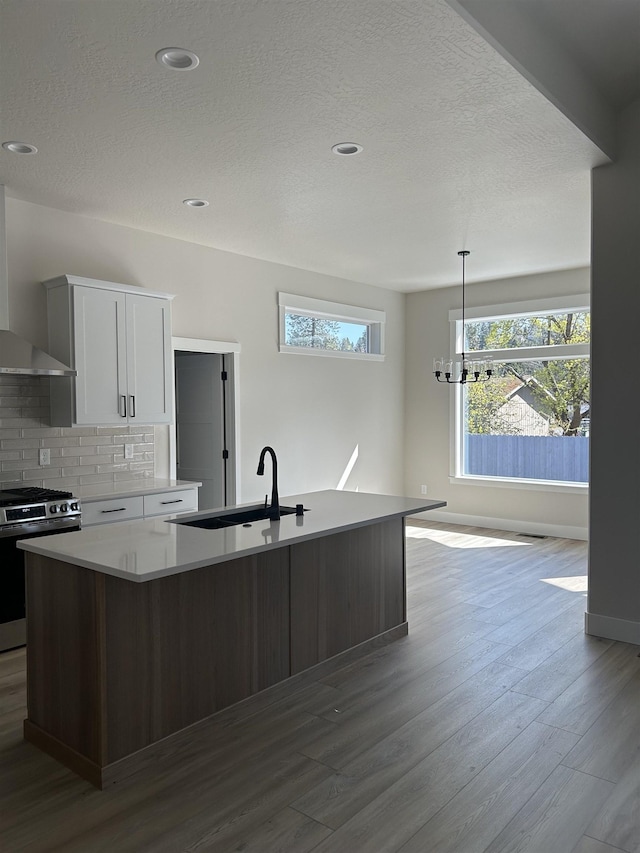 6010 N Windsor St, Spokane, WA 99208 - kitchen featuring dark wood-style flooring, a sink, stainless steel range with gas stovetop, a kitchen island with sink, and wall chimney exhaust hood