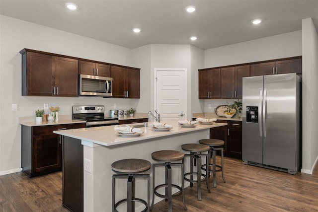 kitchen with a kitchen bar, dark hardwood / wood-style flooring, stainless steel appliances, an island with sink, and sink