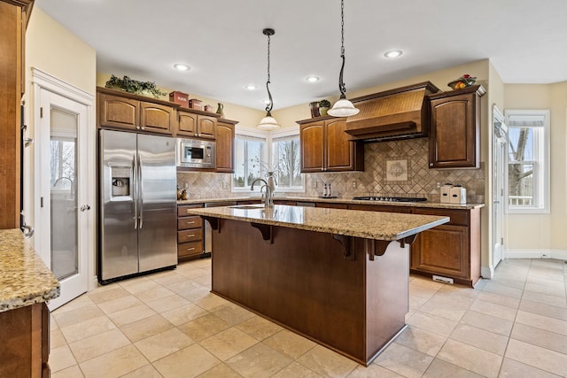 kitchen with light stone countertops, pendant lighting, stainless steel appliances, an island with sink, and a breakfast bar area