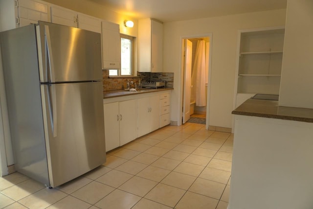 kitchen with decorative backsplash, sink, white cabinetry, light tile patterned floors, and stainless steel fridge