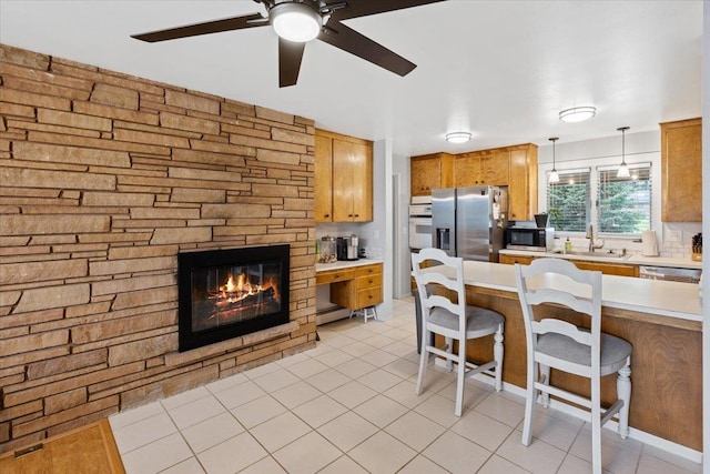 kitchen featuring hanging light fixtures, appliances with stainless steel finishes, sink, a fireplace, and a breakfast bar