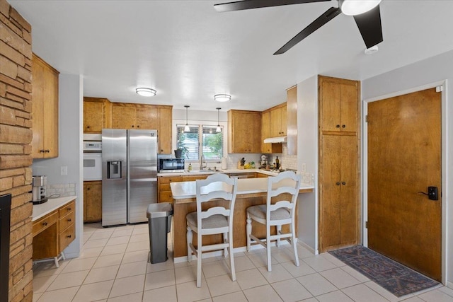 kitchen featuring pendant lighting, backsplash, stainless steel fridge with ice dispenser, oven, and a breakfast bar area