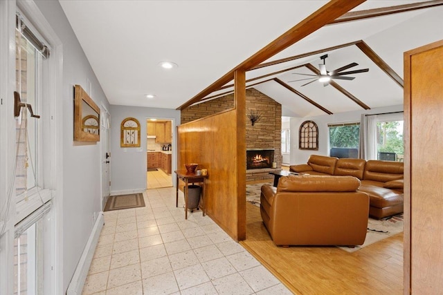 living room with ceiling fan, a stone fireplace, and vaulted ceiling with beams