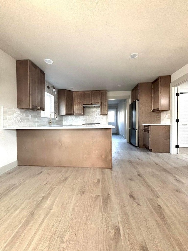 kitchen featuring kitchen peninsula, a healthy amount of sunlight, light hardwood / wood-style flooring, and stainless steel fridge