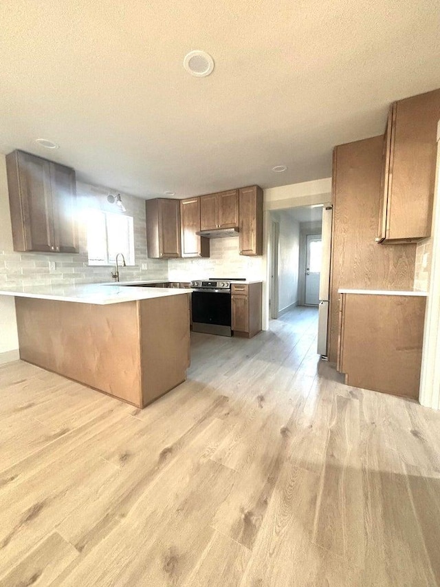 kitchen with kitchen peninsula, sink, stainless steel electric range oven, light wood-type flooring, and a breakfast bar