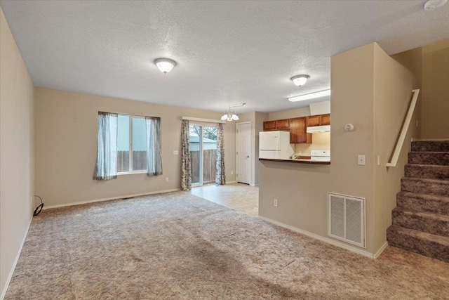 unfurnished living room with a textured ceiling, light carpet, and an inviting chandelier