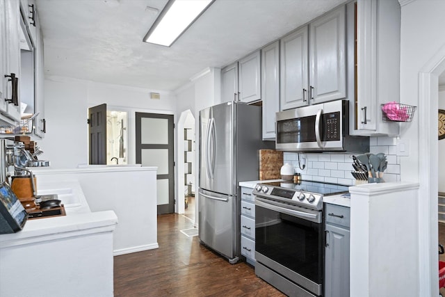 kitchen with appliances with stainless steel finishes, dark wood-type flooring, gray cabinetry, and decorative backsplash