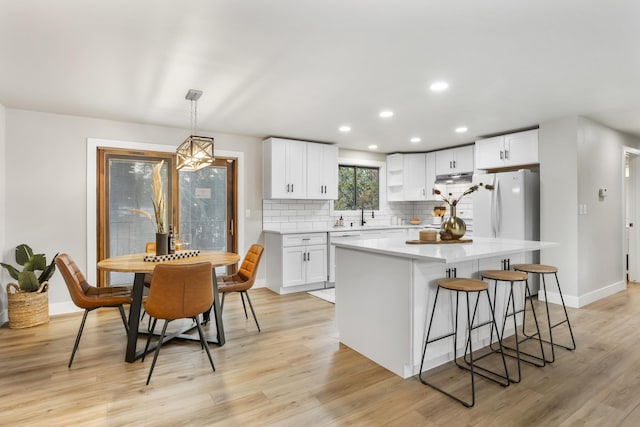 kitchen featuring pendant lighting, white cabinets, a kitchen island, decorative backsplash, and light hardwood / wood-style flooring