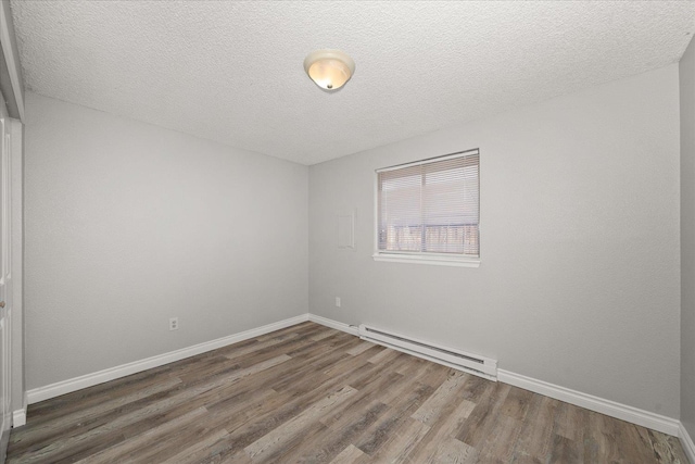 empty room featuring dark hardwood / wood-style floors, baseboard heating, and a textured ceiling