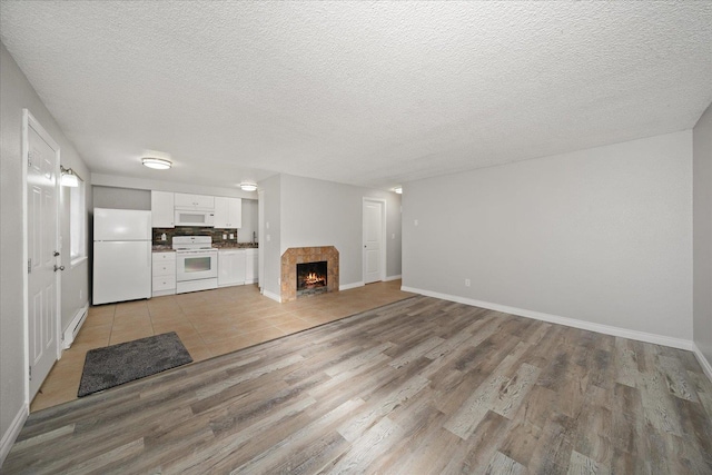 unfurnished living room featuring a baseboard heating unit, light hardwood / wood-style flooring, a tile fireplace, and a textured ceiling