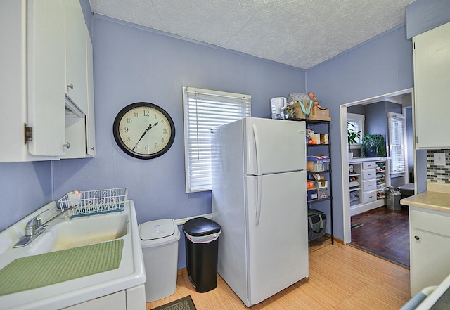 kitchen with sink, white refrigerator, white cabinets, and light hardwood / wood-style flooring