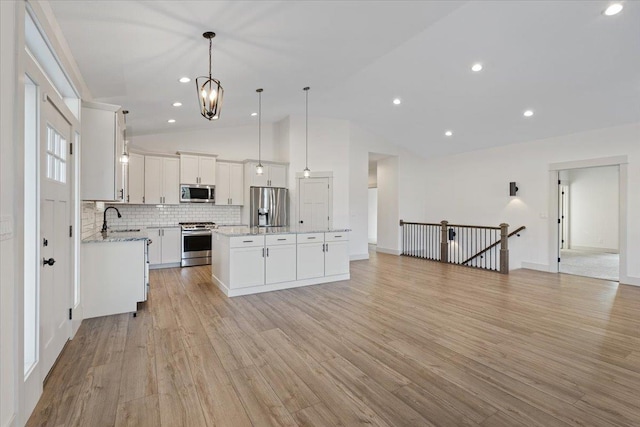 kitchen featuring hanging light fixtures, appliances with stainless steel finishes, white cabinets, a center island, and lofted ceiling