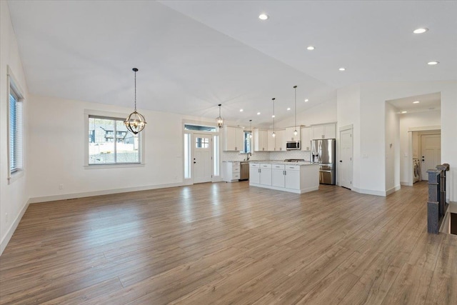 unfurnished living room featuring sink, light hardwood / wood-style flooring, an inviting chandelier, and vaulted ceiling