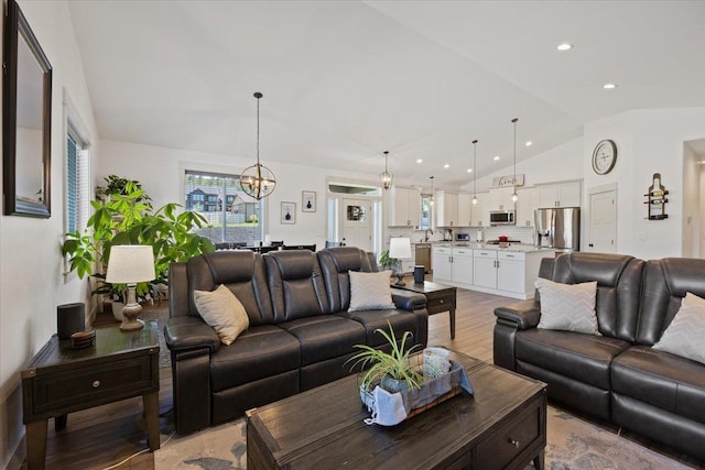 living room with a notable chandelier, vaulted ceiling, and light hardwood / wood-style floors