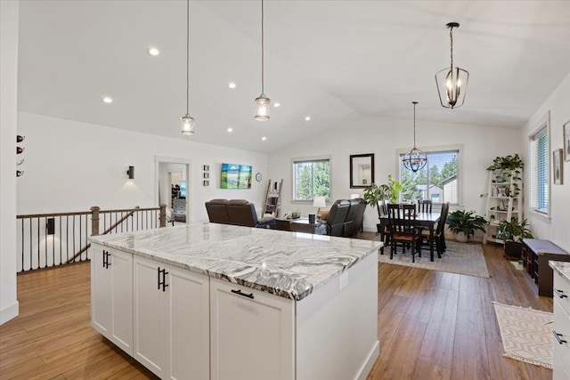 kitchen with white cabinetry, decorative light fixtures, light hardwood / wood-style flooring, light stone counters, and lofted ceiling