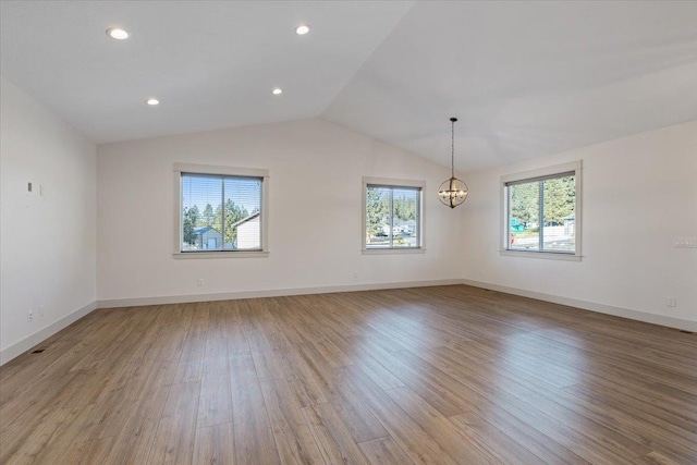 empty room featuring a wealth of natural light, light hardwood / wood-style flooring, a notable chandelier, and vaulted ceiling