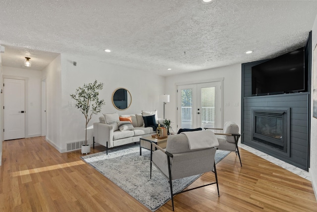 living room featuring a fireplace, a textured ceiling, french doors, and light wood-type flooring