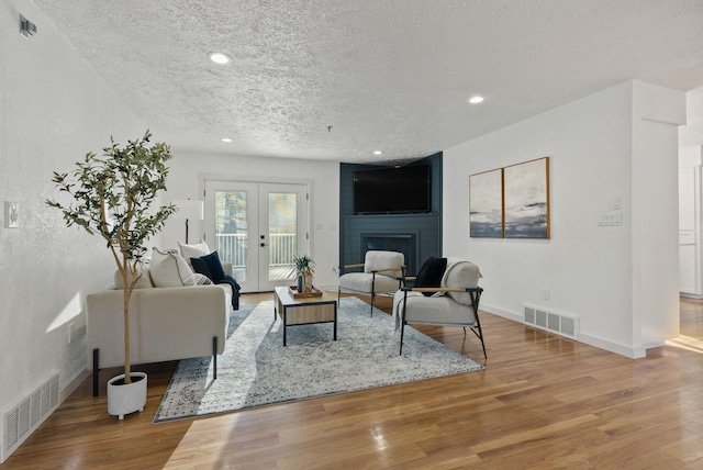 living room featuring a large fireplace, french doors, a textured ceiling, and wood-type flooring