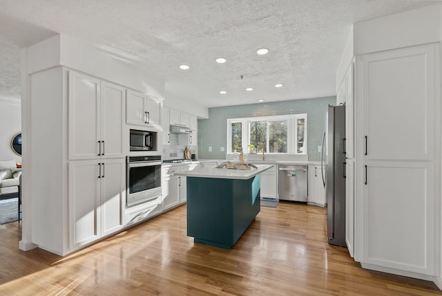 kitchen featuring appliances with stainless steel finishes, white cabinetry, a textured ceiling, a kitchen island, and light hardwood / wood-style floors