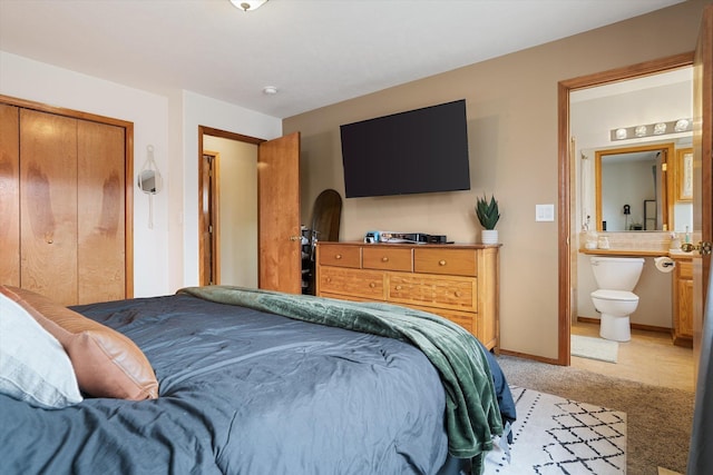 bedroom with a closet, connected bathroom, and light colored carpet