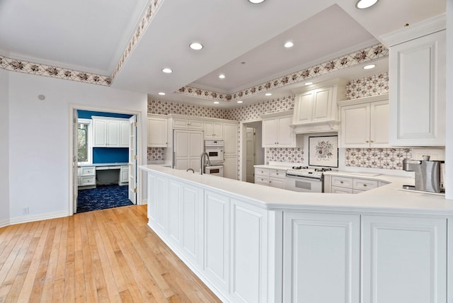 kitchen featuring white appliances, white cabinets, kitchen peninsula, ornamental molding, and light wood-type flooring