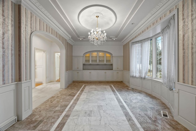 unfurnished dining area with a tray ceiling, a notable chandelier, and ornamental molding