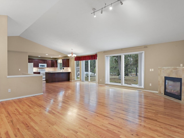 unfurnished living room featuring a tile fireplace, light hardwood / wood-style floors, a chandelier, and lofted ceiling