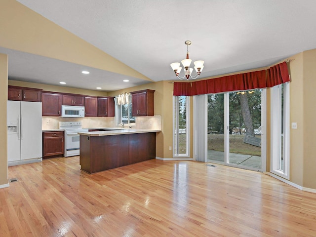 kitchen with white appliances, a chandelier, kitchen peninsula, pendant lighting, and vaulted ceiling