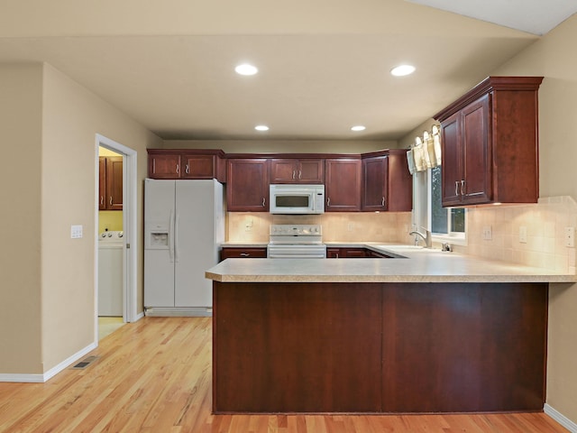 kitchen with washer / dryer, white appliances, sink, light wood-type flooring, and kitchen peninsula