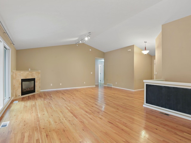 unfurnished living room with lofted ceiling, a healthy amount of sunlight, light hardwood / wood-style floors, rail lighting, and a tiled fireplace