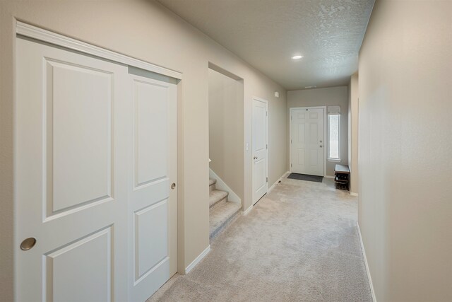 hallway with light carpet and a textured ceiling