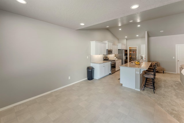 kitchen with appliances with stainless steel finishes, a breakfast bar, white cabinetry, a kitchen island with sink, and light stone counters