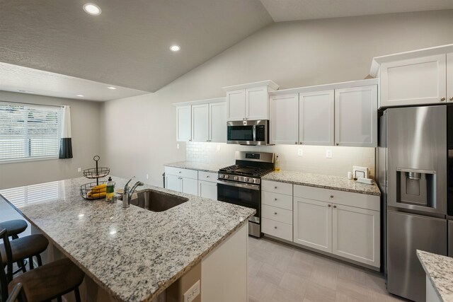 kitchen with sink, appliances with stainless steel finishes, an island with sink, light stone countertops, and white cabinets