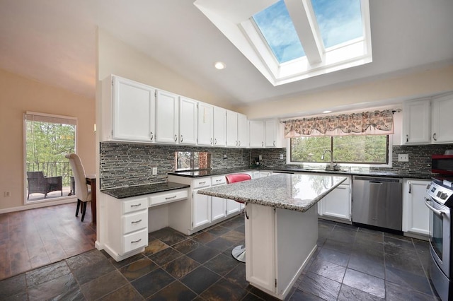 kitchen featuring appliances with stainless steel finishes, plenty of natural light, white cabinetry, vaulted ceiling with skylight, and a center island