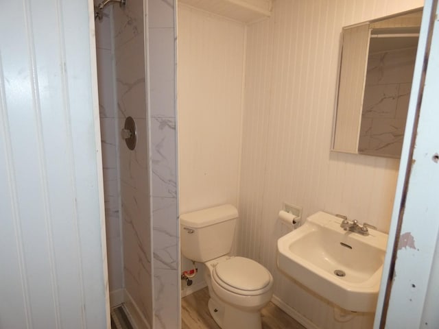 bathroom with wood-type flooring, toilet, sink, and a tile shower