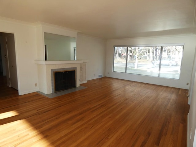 unfurnished living room featuring hardwood / wood-style flooring, crown molding, and a tiled fireplace