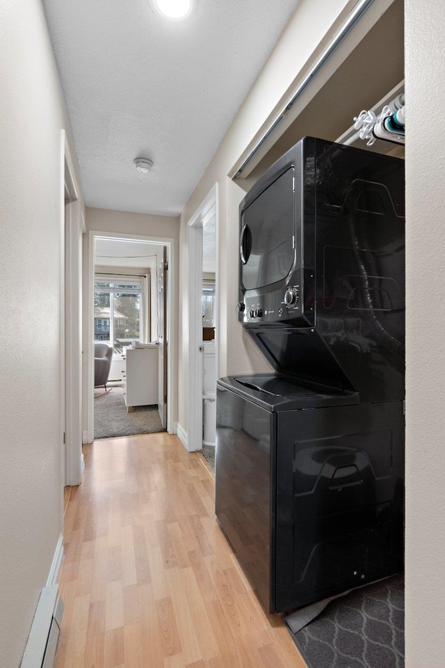 clothes washing area featuring baseboard heating, stacked washer and clothes dryer, and light hardwood / wood-style floors