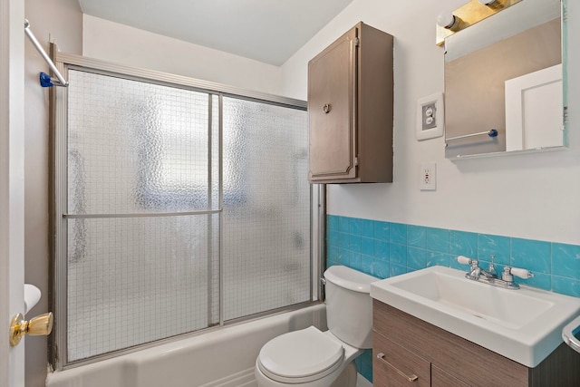 full bathroom featuring bath / shower combo with glass door, tile walls, vanity, and toilet