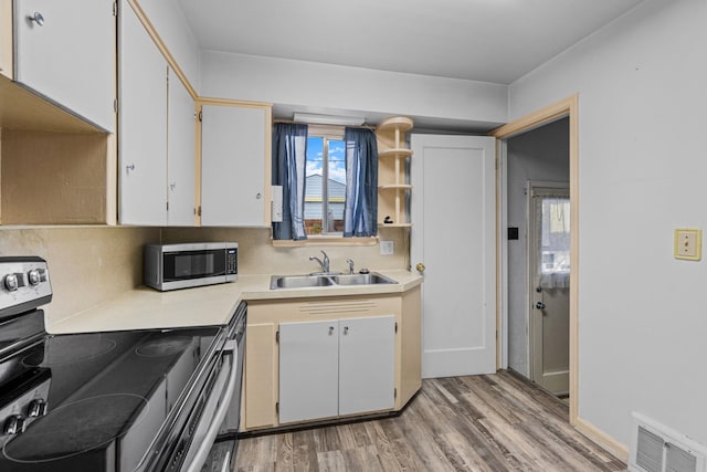 kitchen with stainless steel appliances, sink, white cabinets, and light hardwood / wood-style floors