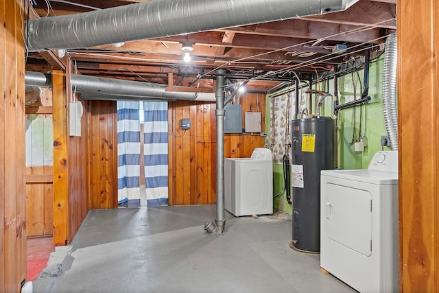 basement with washer and clothes dryer, electric water heater, and wood walls