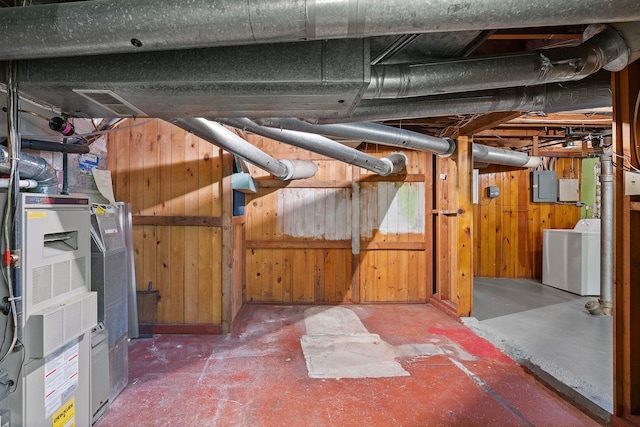 basement featuring electric panel, washer and dryer, and wood walls