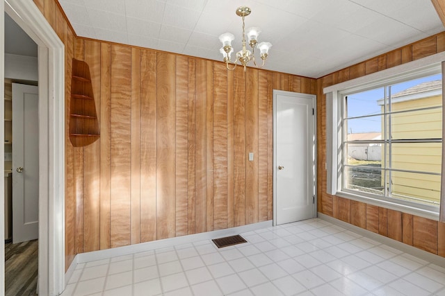 spare room featuring a notable chandelier, a wealth of natural light, and wood walls